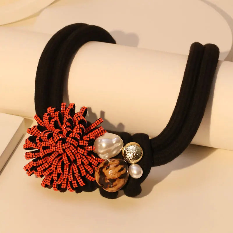 Kaulakoru, jossa on punainen kukka-riipus ja helmiä